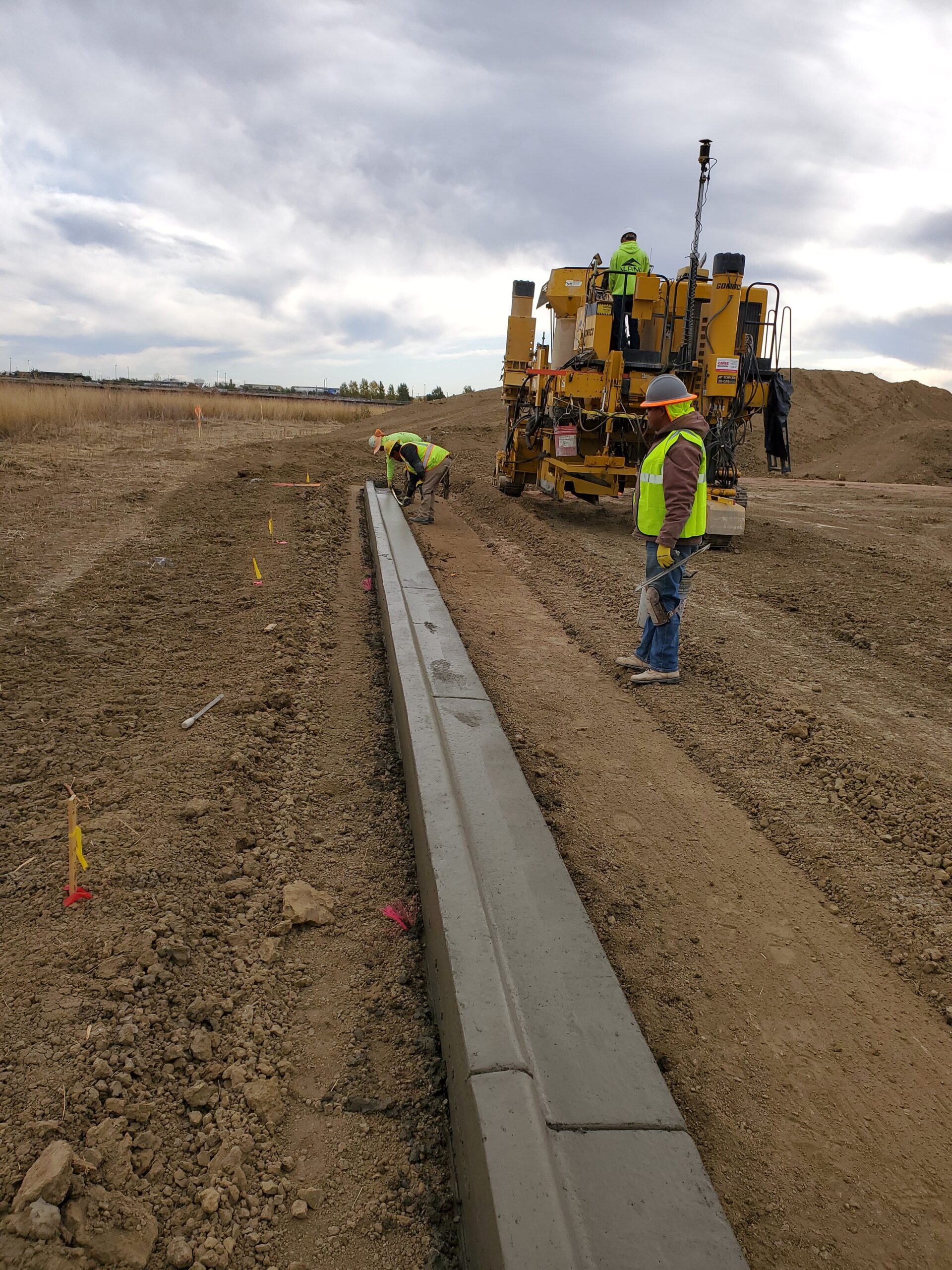 Construction workers installing concrete curb and gutter using a curb machine at an active roadway development project.