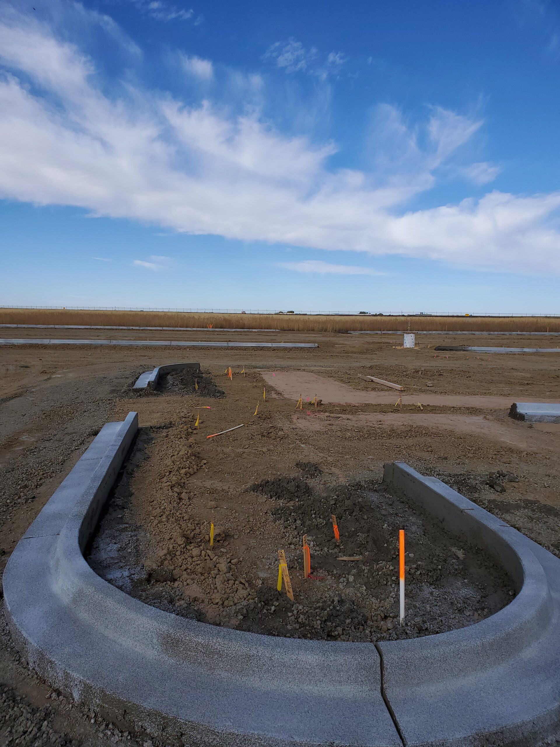 Curved concrete curb and gutter installed at a developing construction site with survey stakes marking the layout.