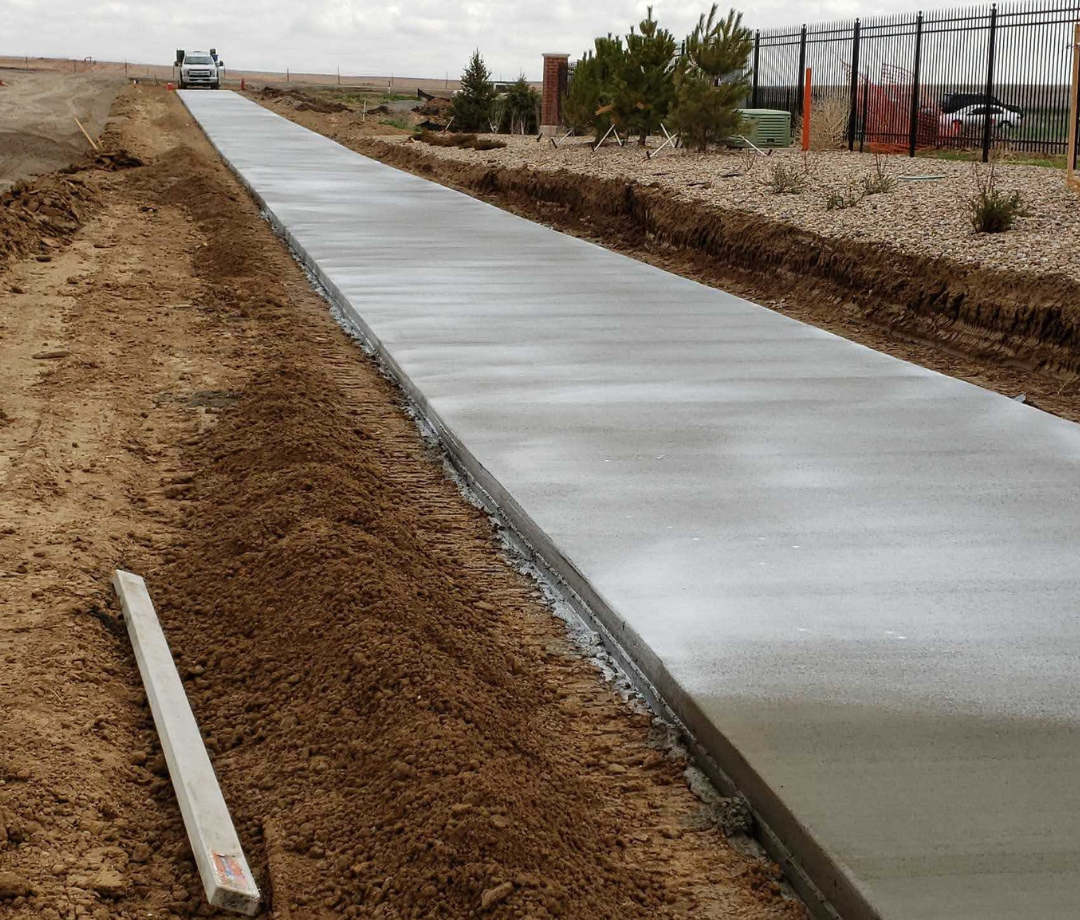 Freshly poured concrete sidewalk during the 17th Avenue Sidewalk Improvement Project with soil grading and landscaping along the path.