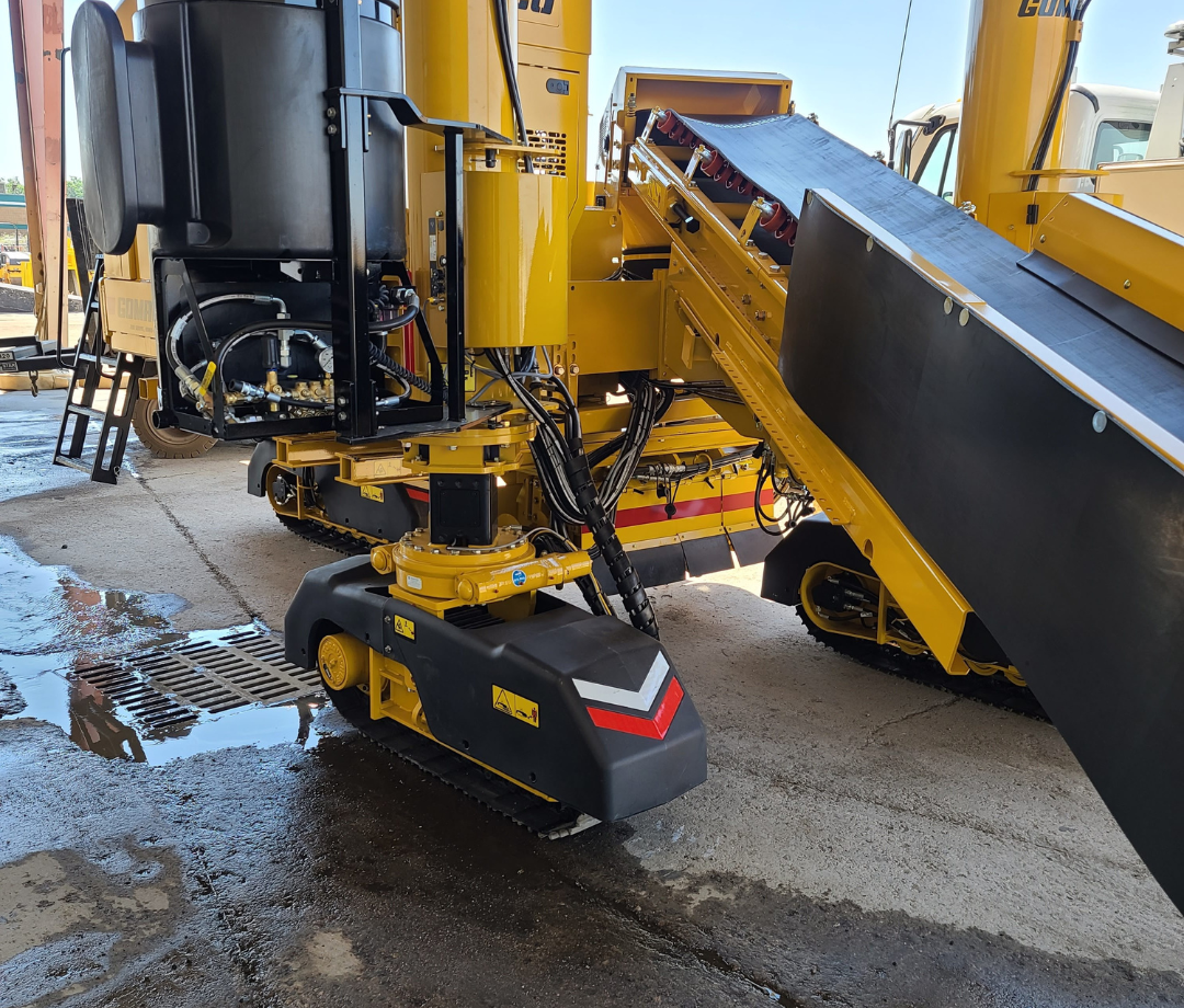 Close-up of specialized road construction equipment with conveyor system used for asphalt paving and material transfer.