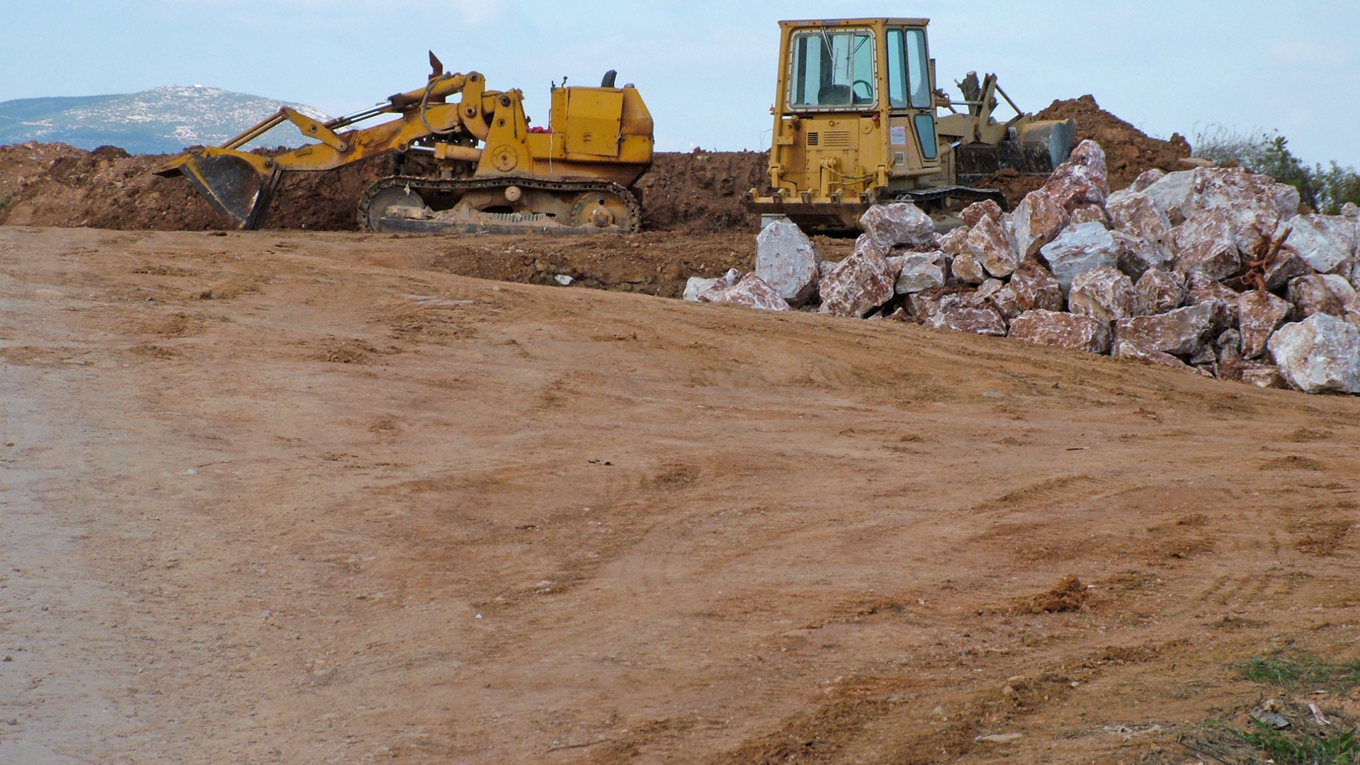 Crawler loader and bulldozer moving soil and large rocks during earthmoving operations at a construction site.