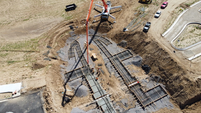 Aerial view of a crane pouring concrete into reinforced formwork for a large structural foundation at an active construction site.