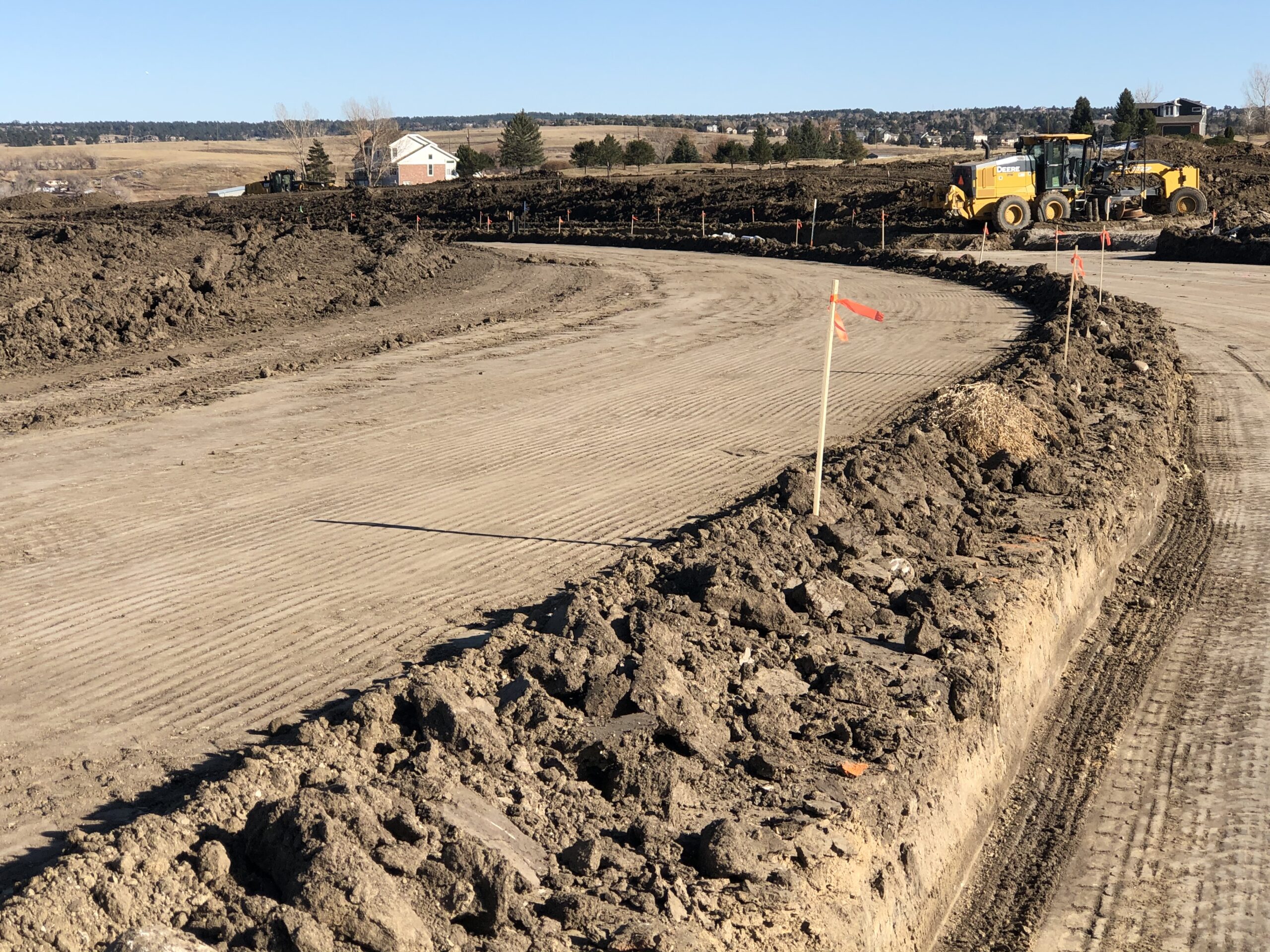 Motor grader shaping and leveling a compacted dirt roadway during site development at a residential construction site.