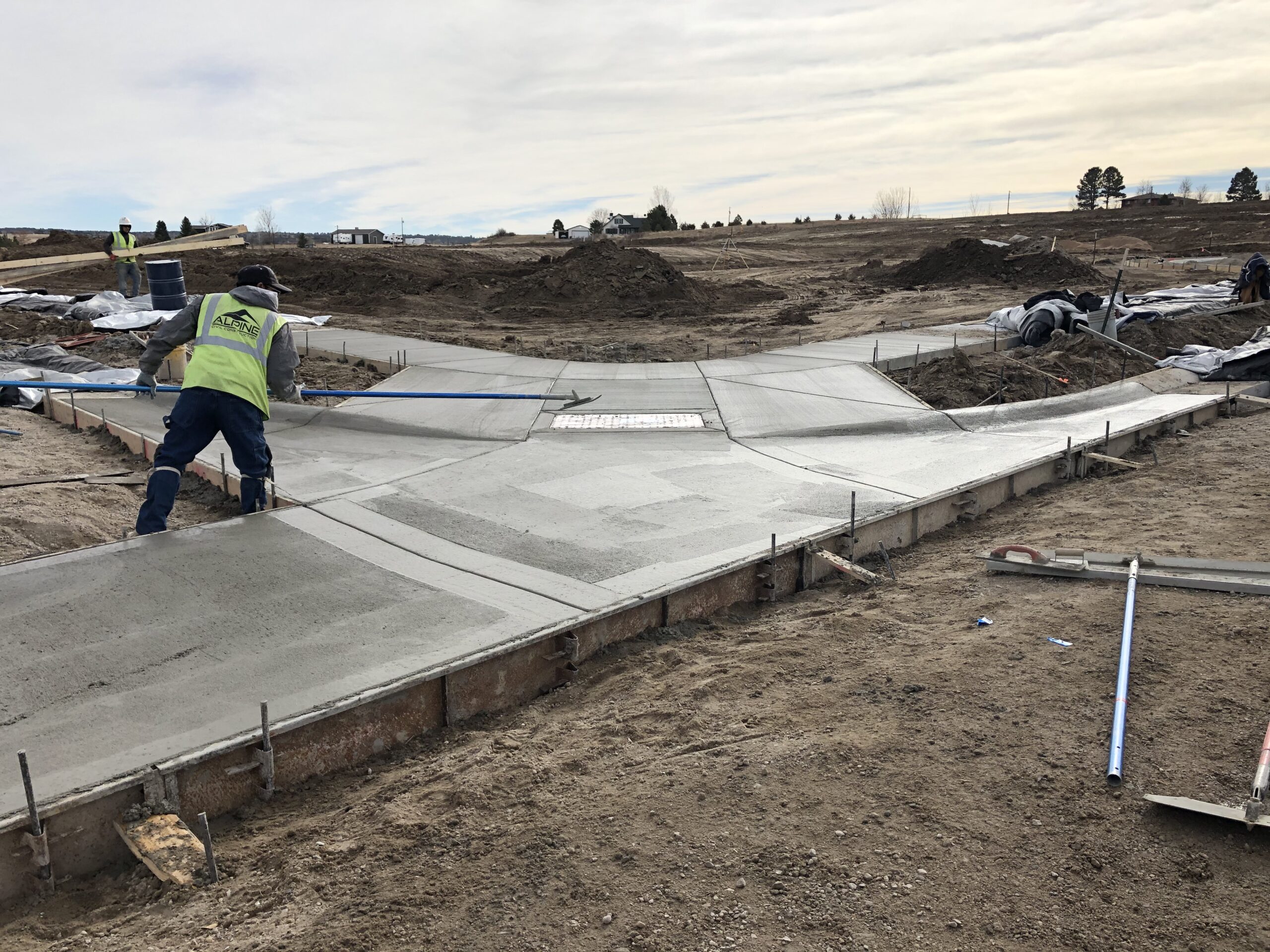 Construction worker finishing newly poured concrete at an intersection with fresh curb ramps and sidewalks under construction.