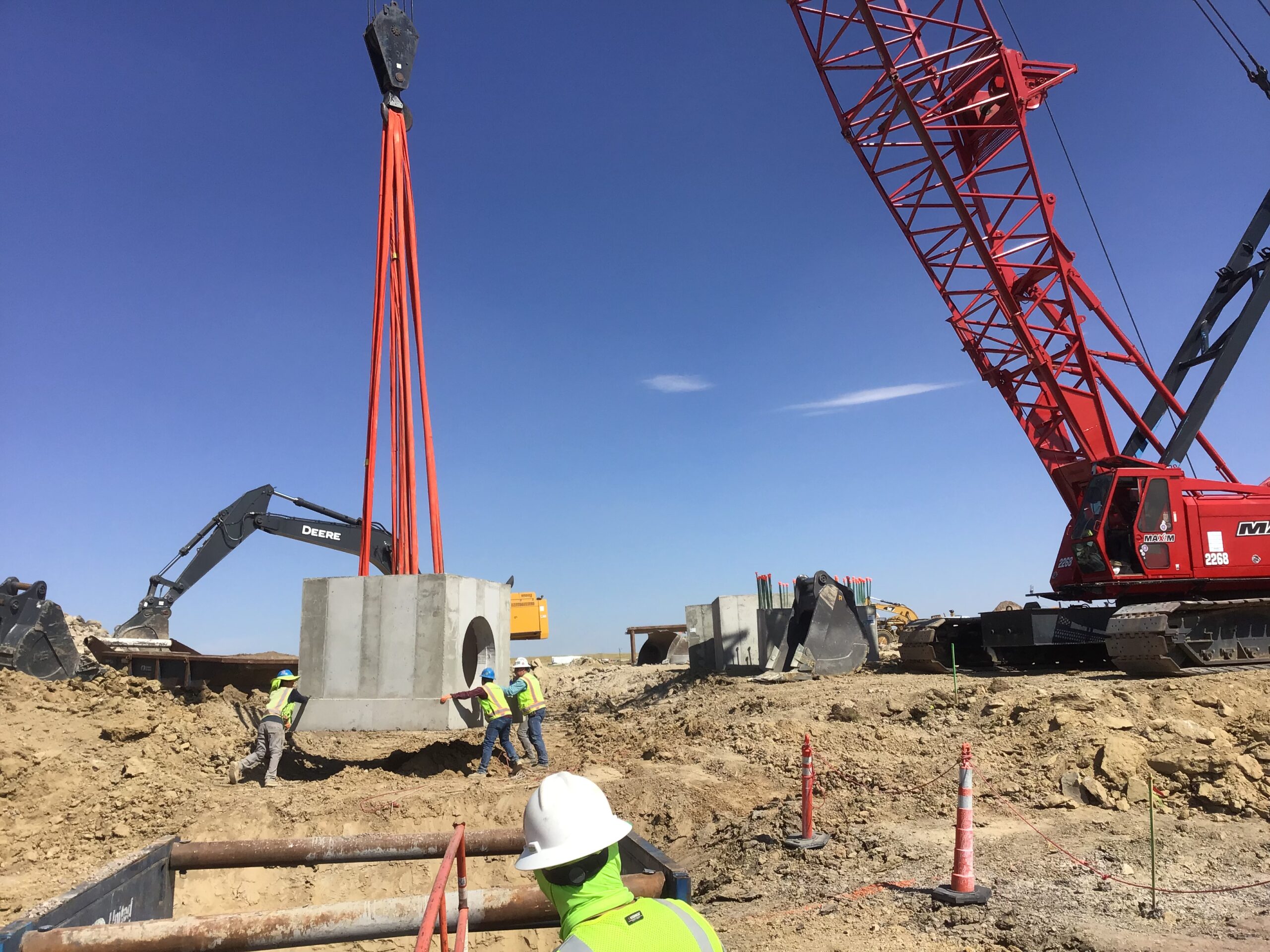 Workers guiding suspended concrete culvert section into place