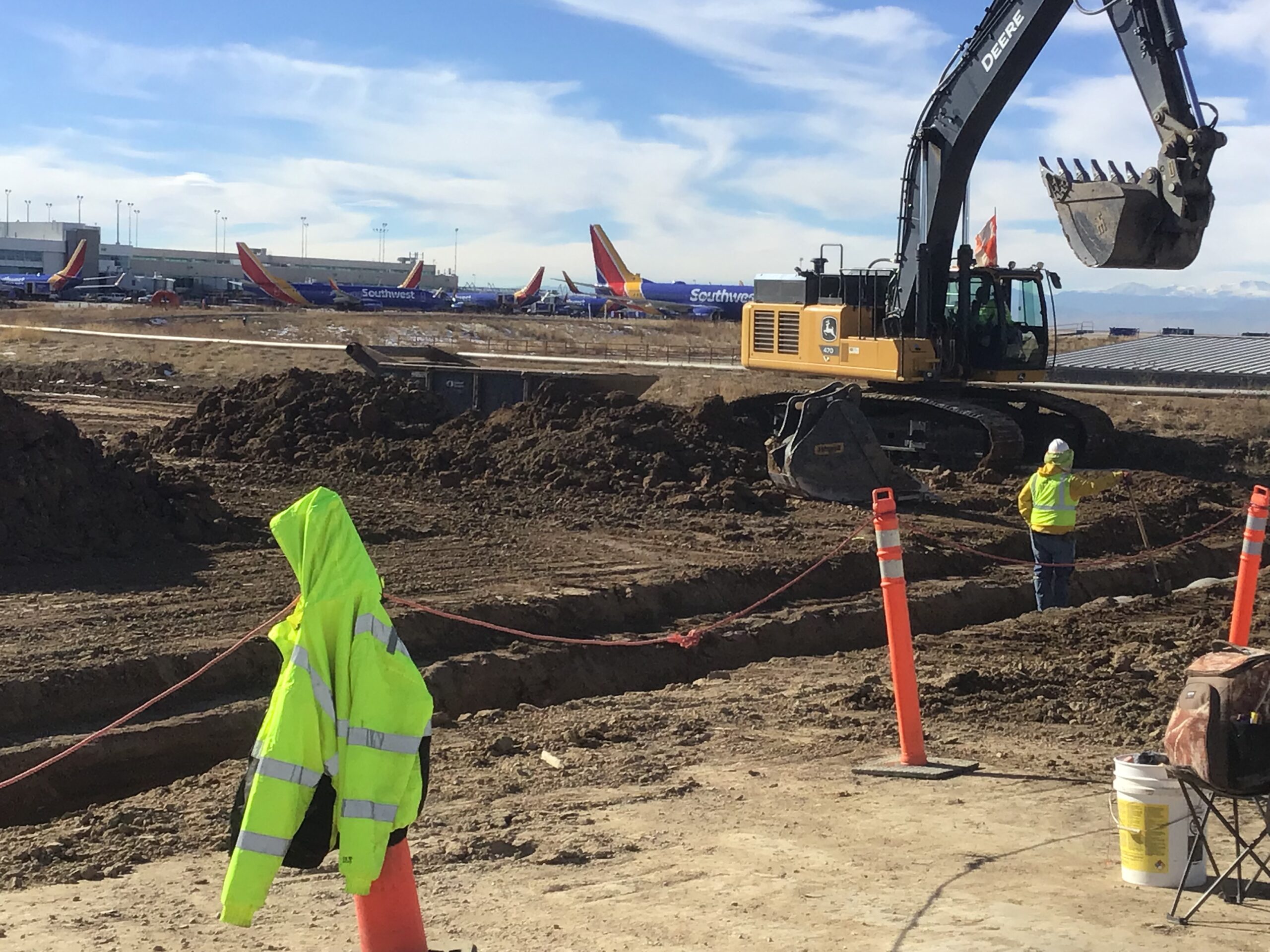 Excavator working near airport runway with planes in background