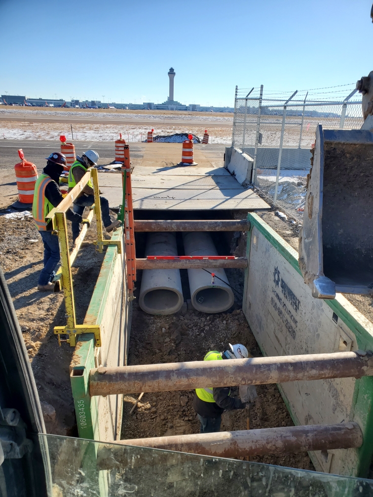 Utility crew working in trench near airport with control tower visible