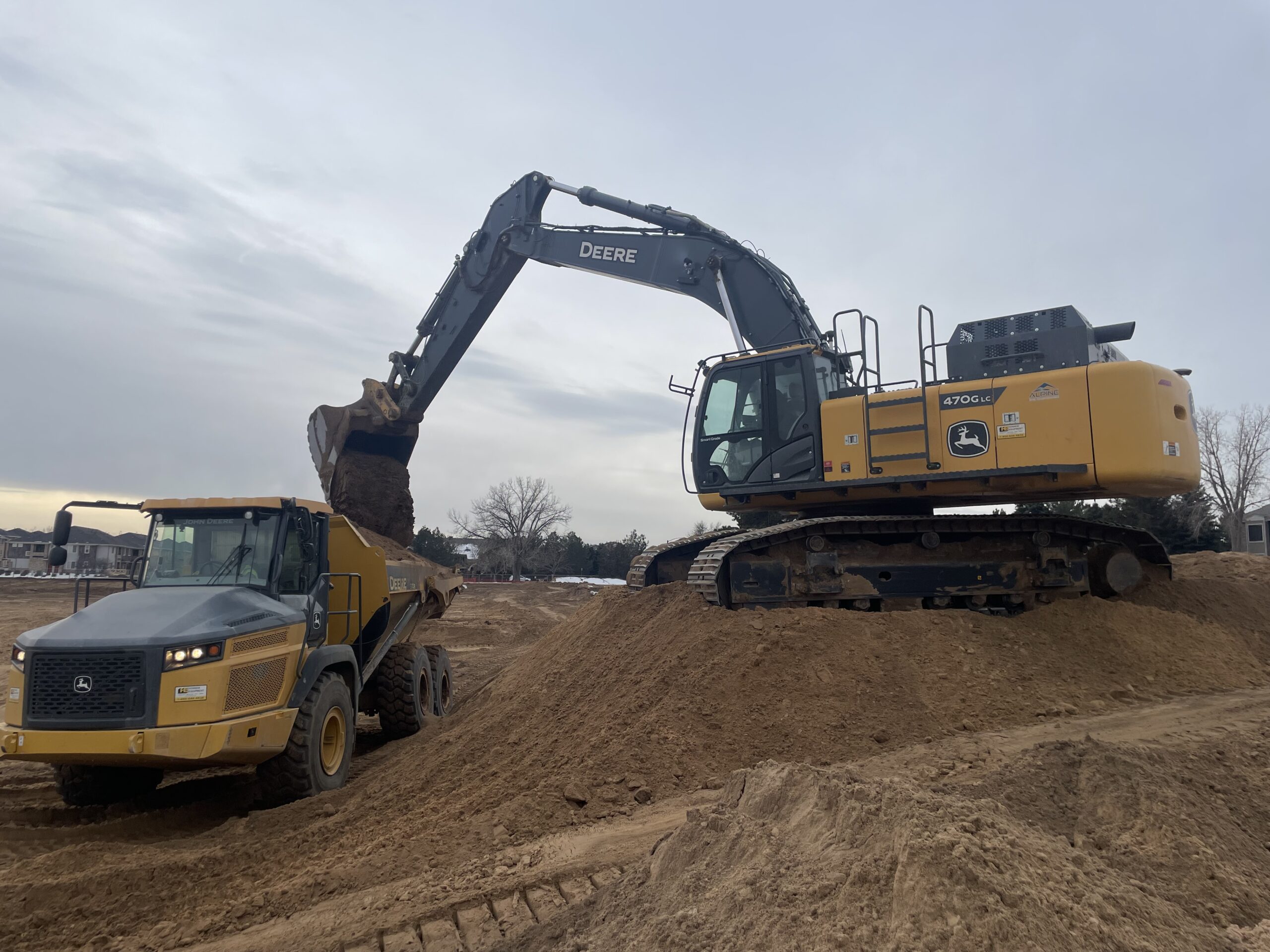 John Deere excavator loading soil into an articulated dump truck during earthmoving operations at a development site.