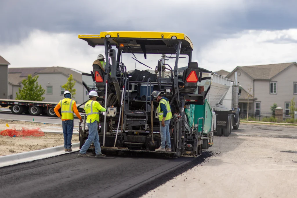 Crew paving a new roadway with an asphalt paver on a residential construction site.